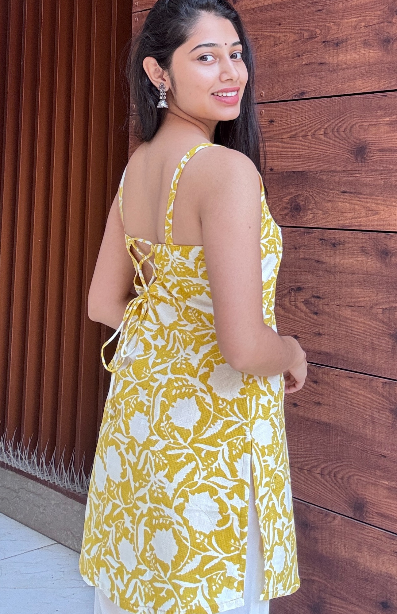 Woman wearing a yellow floral dress against a wooden wall.