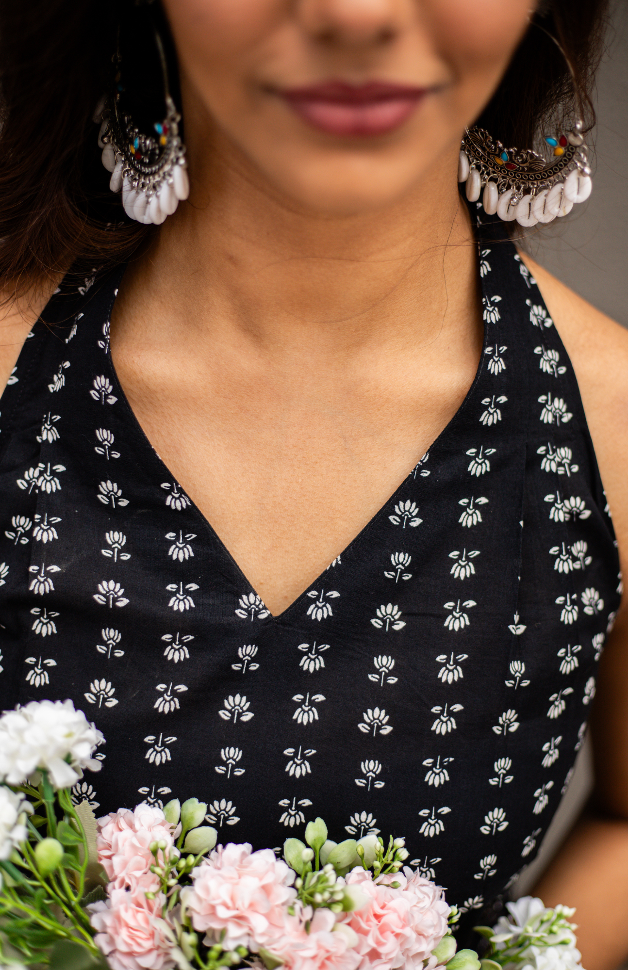 Woman wearing a black dress with white floral pattern, holding flowers.