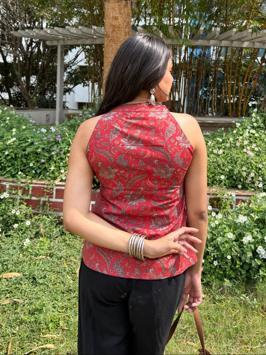 Woman in a red sleeveless top standing in a garden with trees and plants around.
